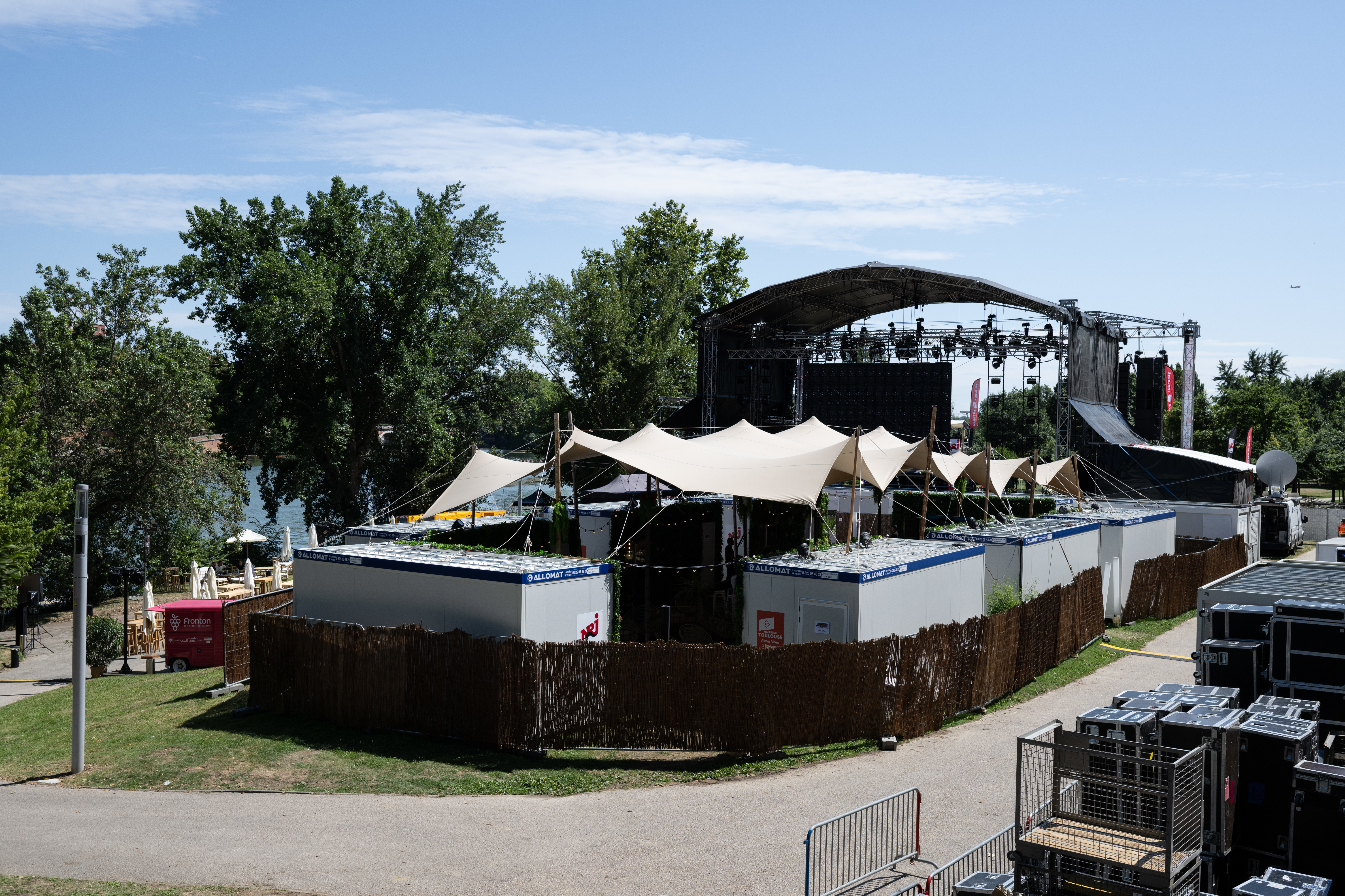 Une vision d'ensemble du backstage des NRJ Music Tour de Toulouse. On y voit des tentes et des modules ALLOMAT sur le devant et la grande scène dans le fond.