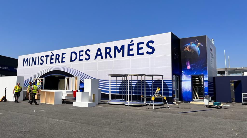 Un bâtiment temporaire du ministère des armées, fait en constructions modulaires. Il sont recouverts avec un habillage bleu et blanc avec des une entrée en forme de vague et l'inscription "Ministère des armées" écrit en bleu sur blanc