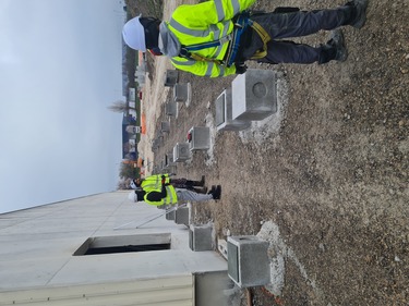 3 ouvriers parmi des plots en bétons qui serviront à installer une construction modulaire attenante à une usine